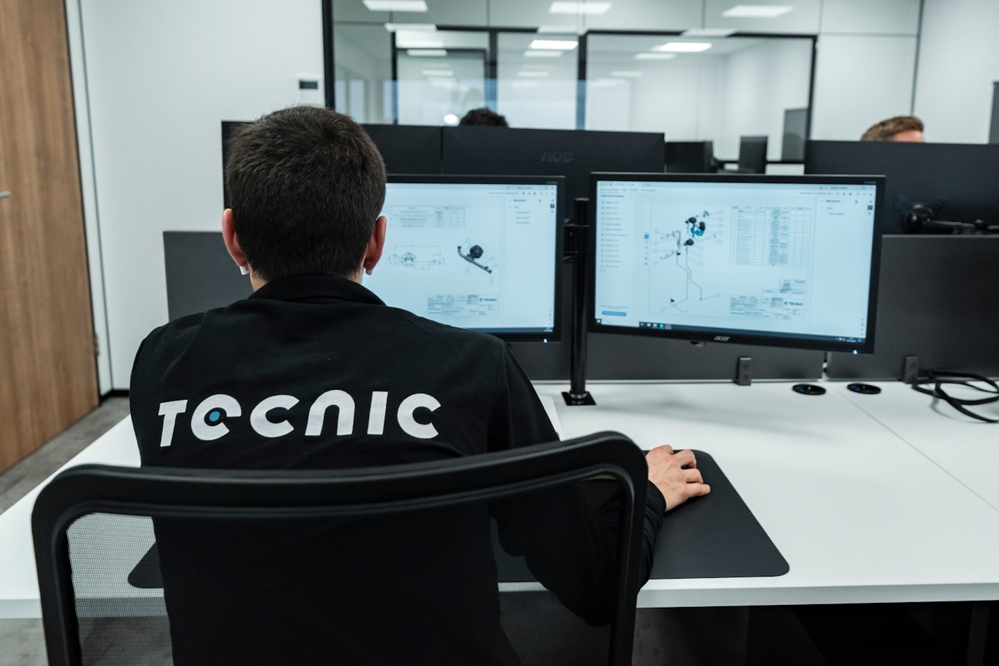 Professional working on CAD software at a dual monitor workstation.